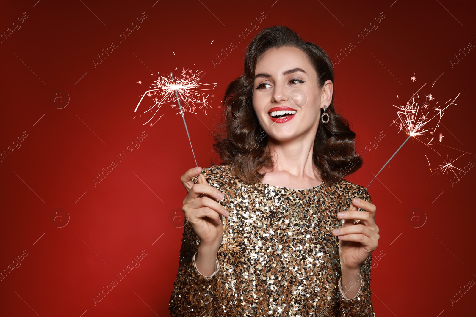 Photo of Smiling woman with sparklers celebrating Christmas on red background