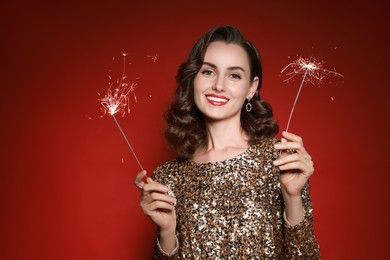 Photo of Smiling woman with sparklers celebrating Christmas on red background