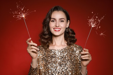 Photo of Smiling woman with sparklers celebrating Christmas on red background