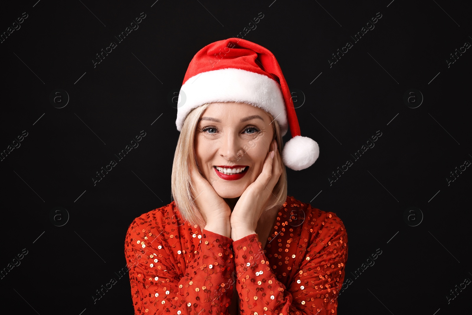 Photo of Smiling woman with perfect makeup in Santa hat celebrating Christmas on black background