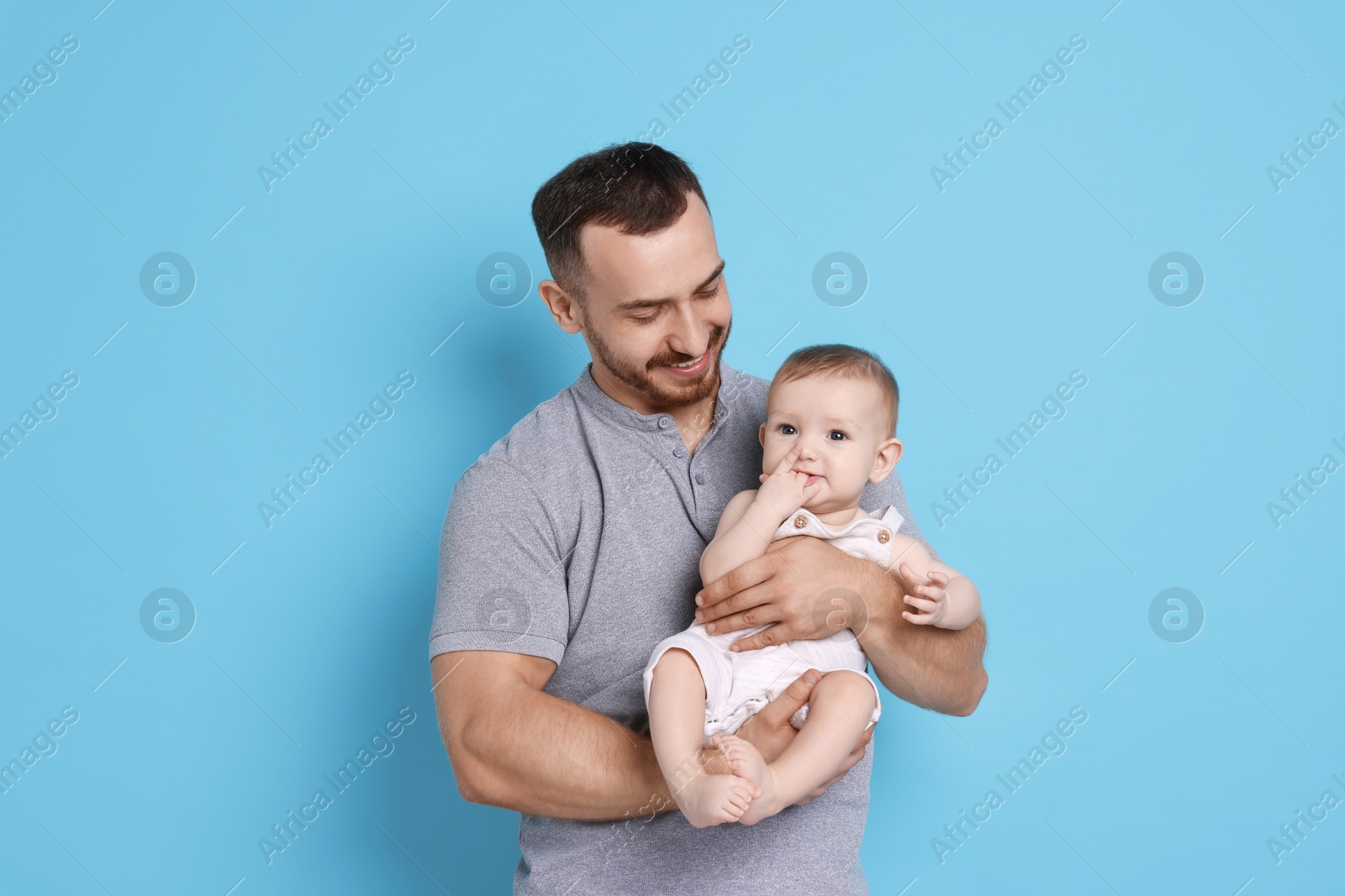 Photo of Father with his cute baby on light blue background