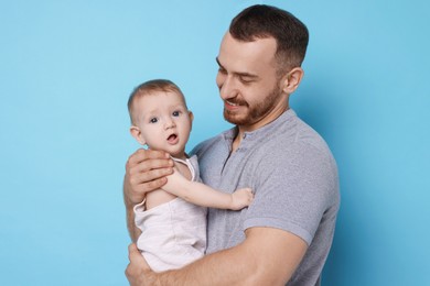 Photo of Father with his cute baby on light blue background