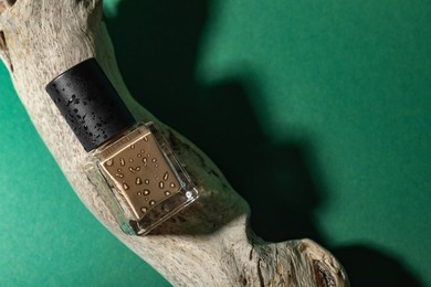 Photo of Nail polish in bottle and piece of decorative wood on green background, top view