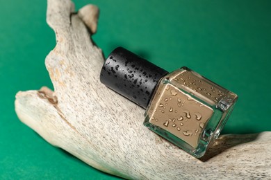 Photo of Nail polish in bottle and piece of decorative wood on green background, closeup