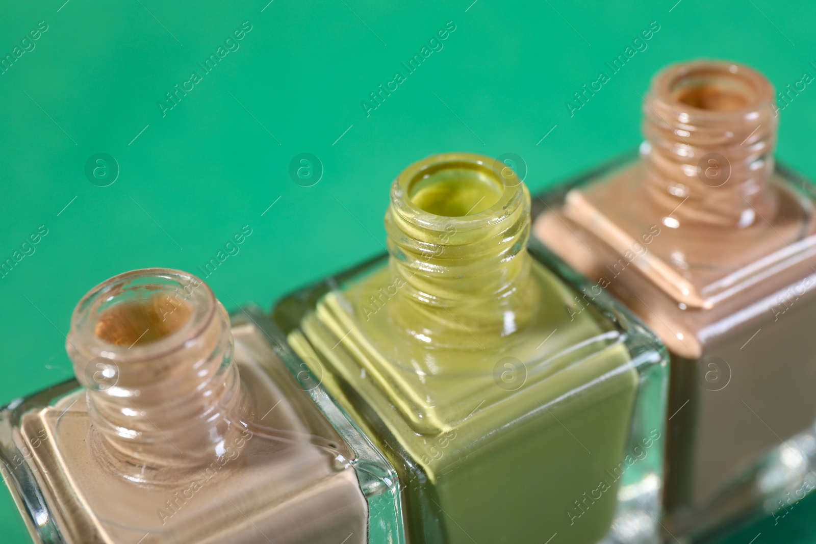 Photo of Nail polishes in bottles on green background, closeup