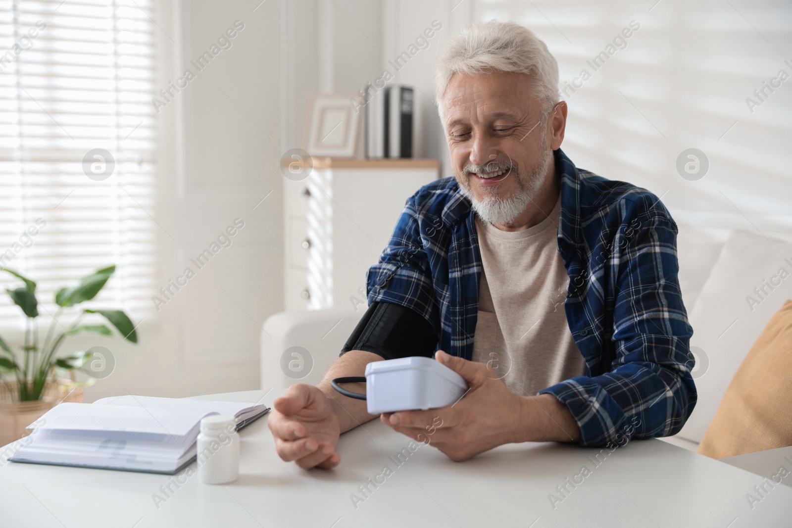 Photo of Senior man measuring blood pressure at table indoors