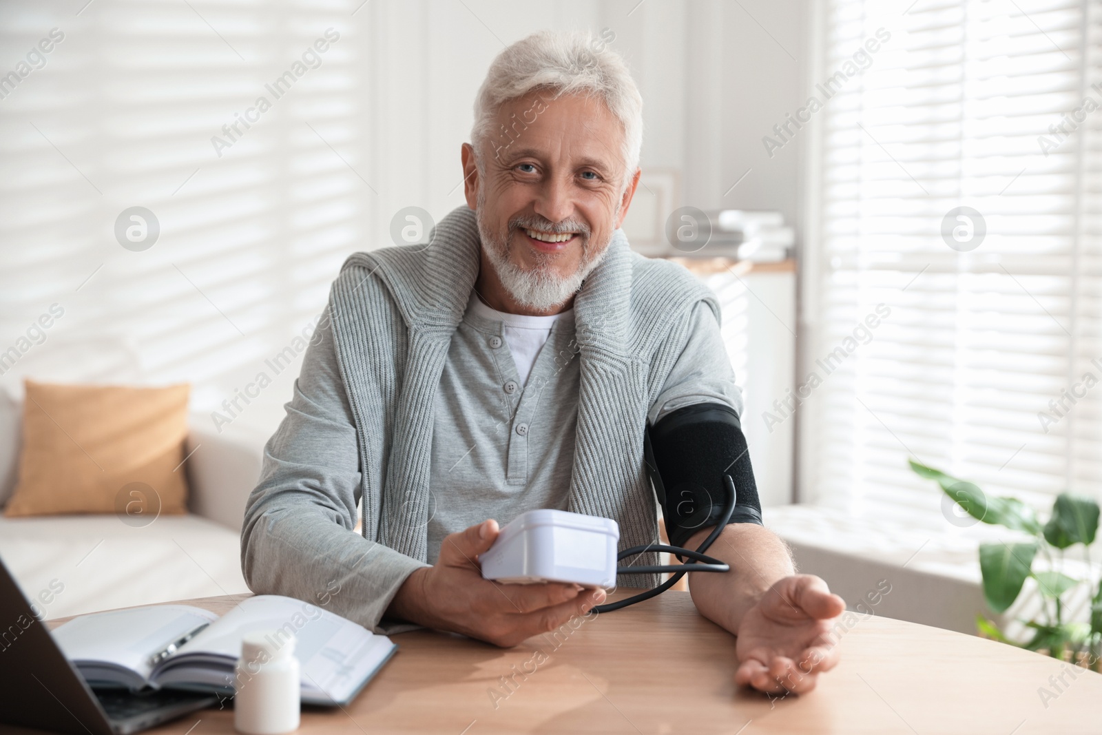 Photo of Senior man measuring blood pressure at wooden table indoors