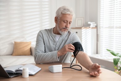 Photo of Senior man measuring blood pressure at wooden table indoors