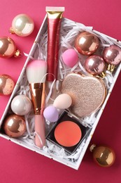 Photo of Christmas present. Decorative cosmetics in gift box and festive balls on dark pink background, top view