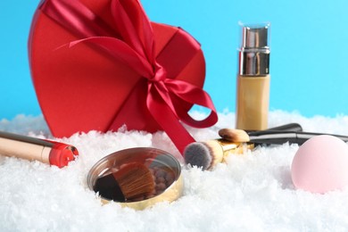 Photo of Christmas present. Decorative cosmetics and gift box on snow against light blue background