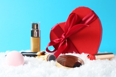 Photo of Christmas present. Decorative cosmetics and gift box on snow against light blue background