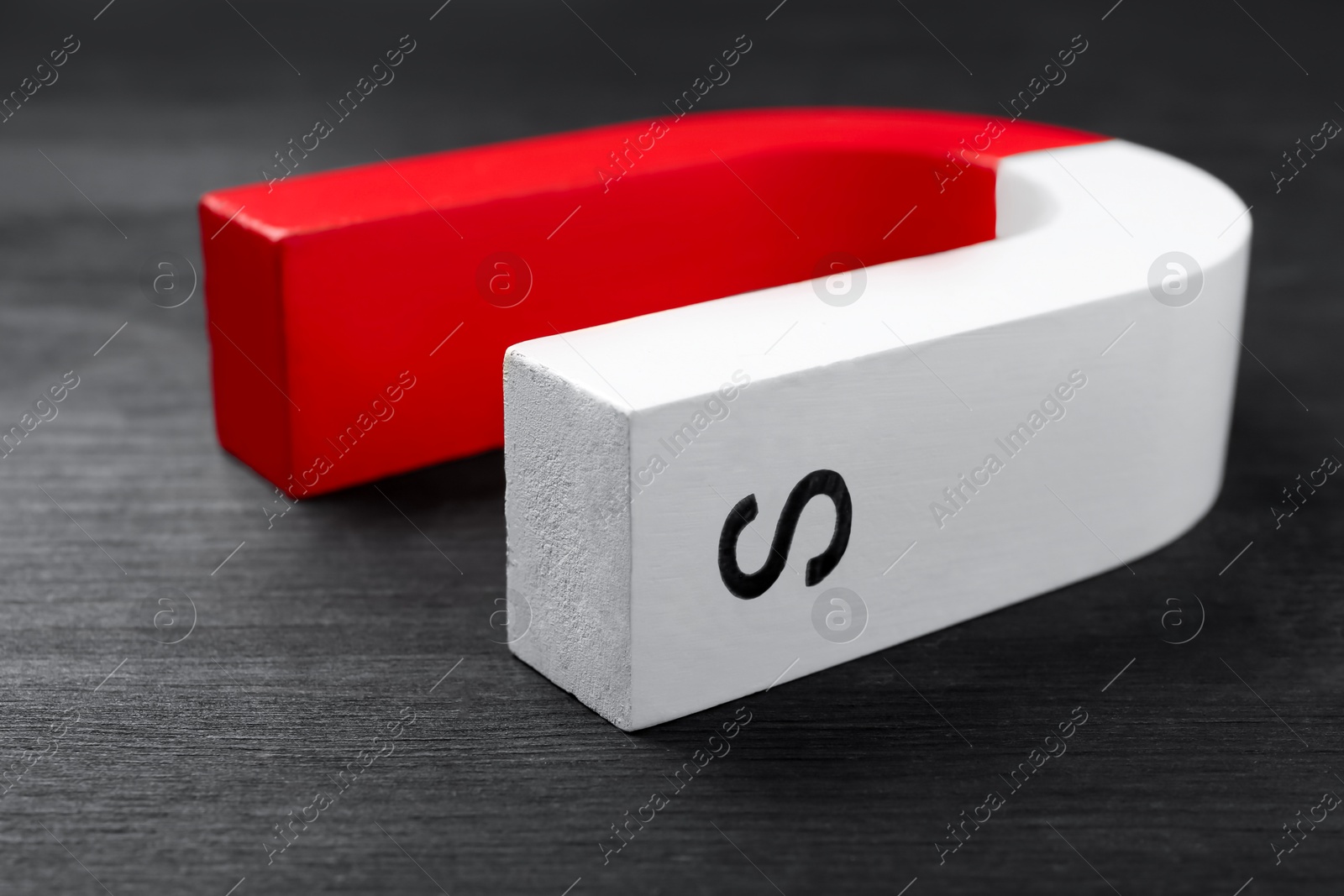 Photo of One horseshoe magnet on black wooden table, closeup