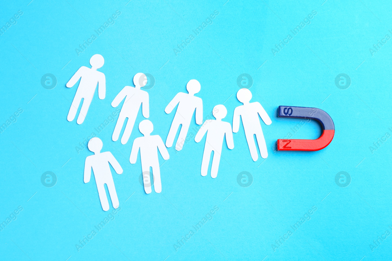 Photo of Magnet attracting paper cutouts of humans on light blue background, flat lay