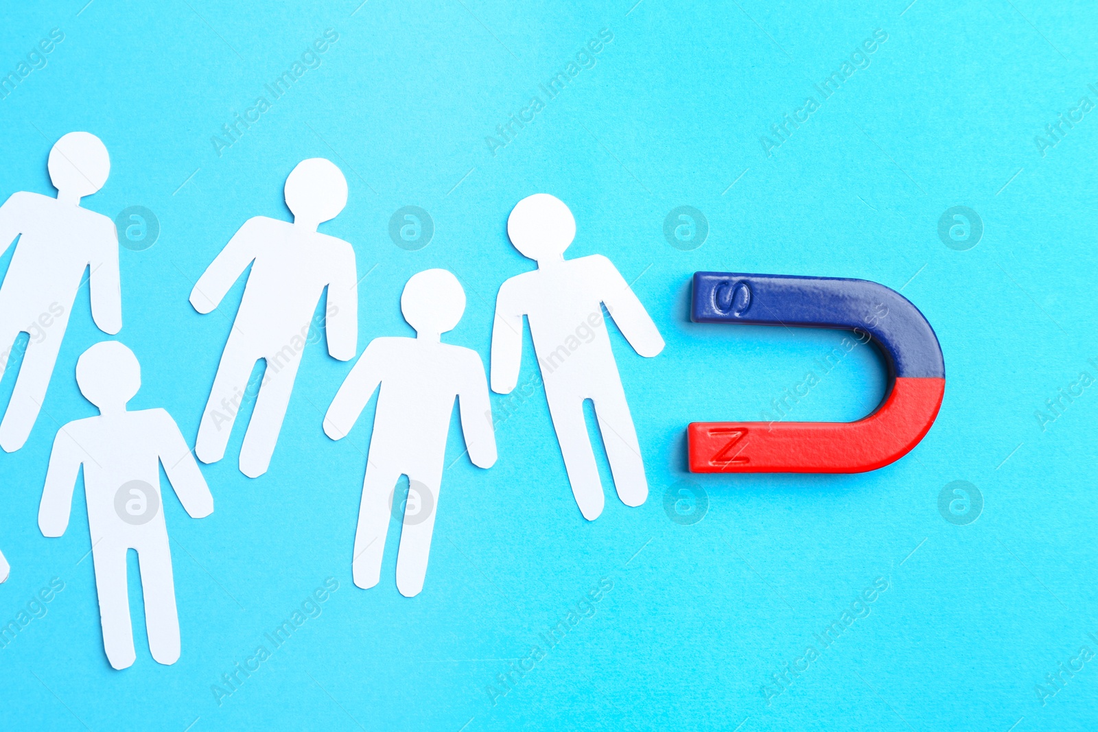 Photo of Magnet attracting paper cutouts of humans on light blue background, flat lay