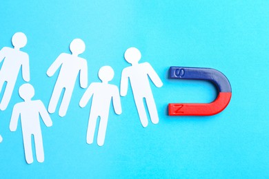 Photo of Magnet attracting paper cutouts of humans on light blue background, flat lay