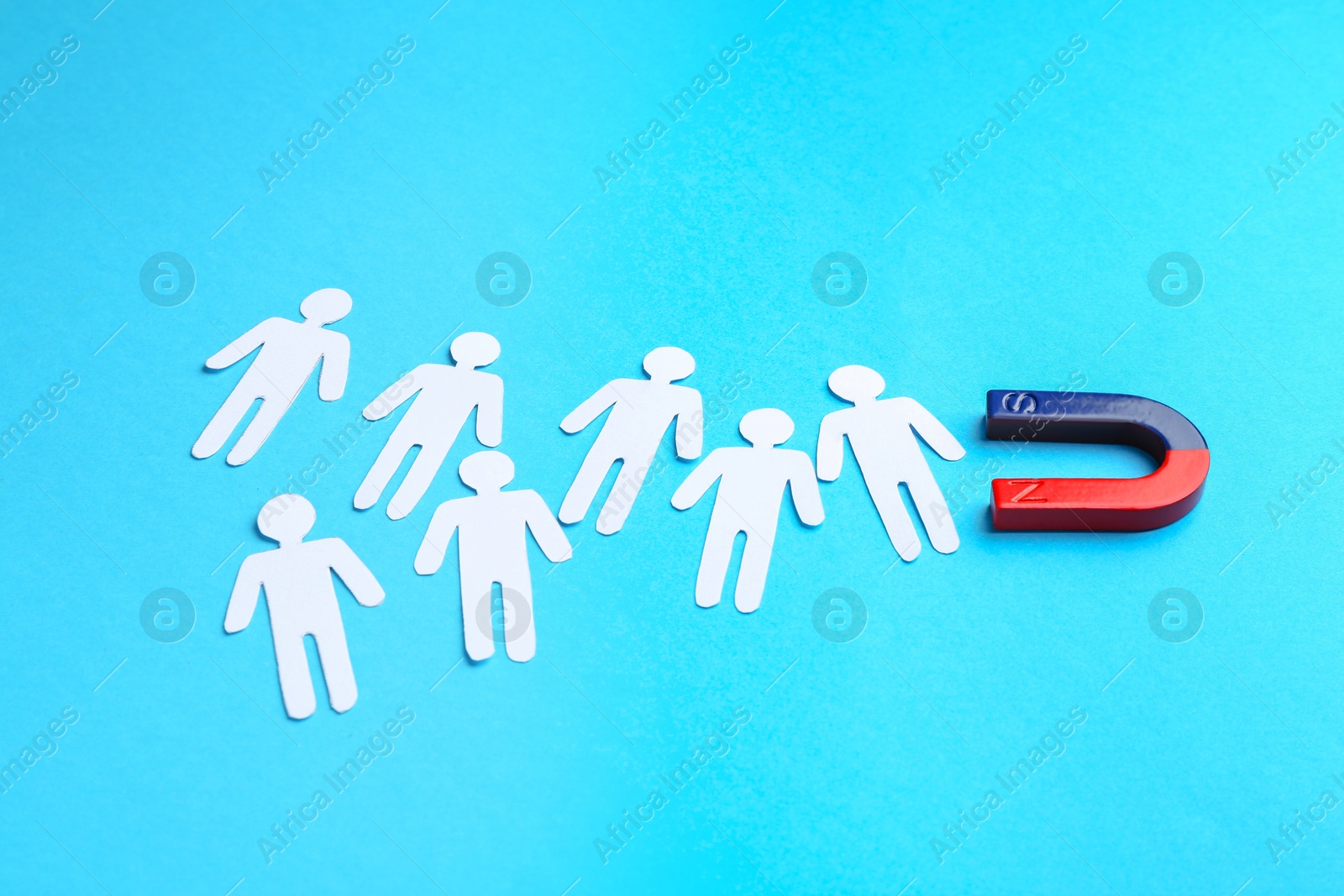 Photo of Magnet attracting paper cutouts of humans on light blue background