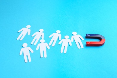 Photo of Magnet attracting paper cutouts of humans on light blue background