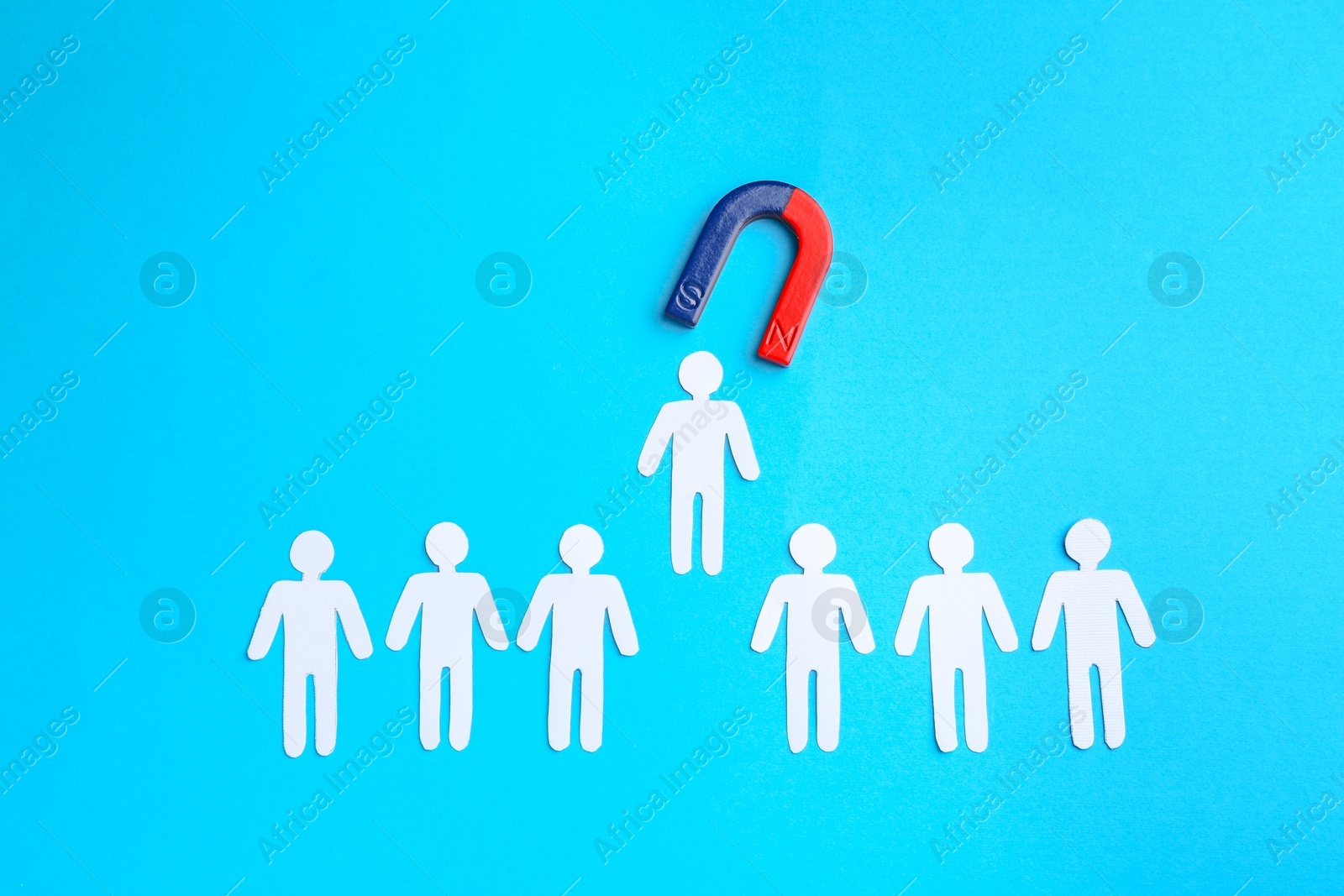 Photo of Magnet attracting paper cutouts of humans on light blue background, flat lay