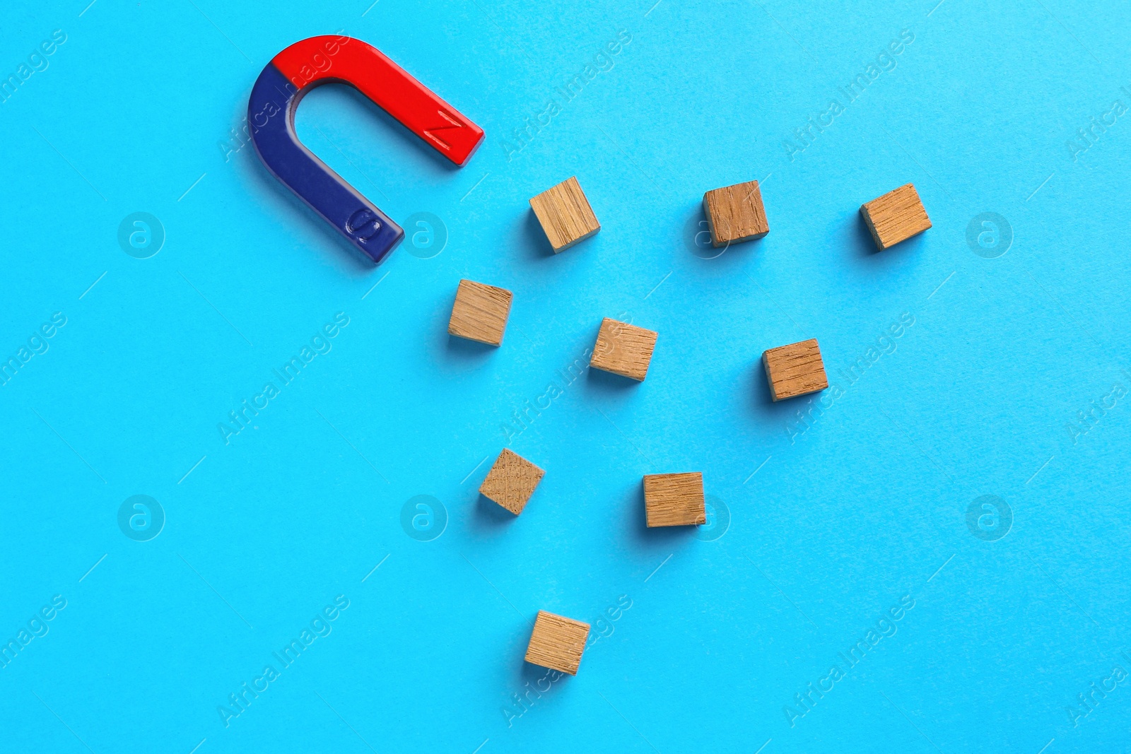 Photo of Magnet attracting wooden cubes on light blue background, flat lay