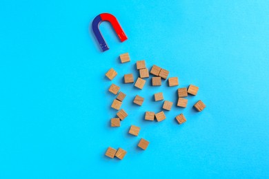 Photo of Magnet attracting wooden cubes on light blue background, flat lay