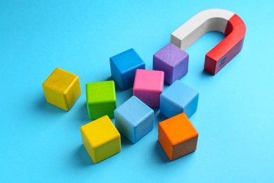 Photo of Magnet attracting colorful cubes on light blue background