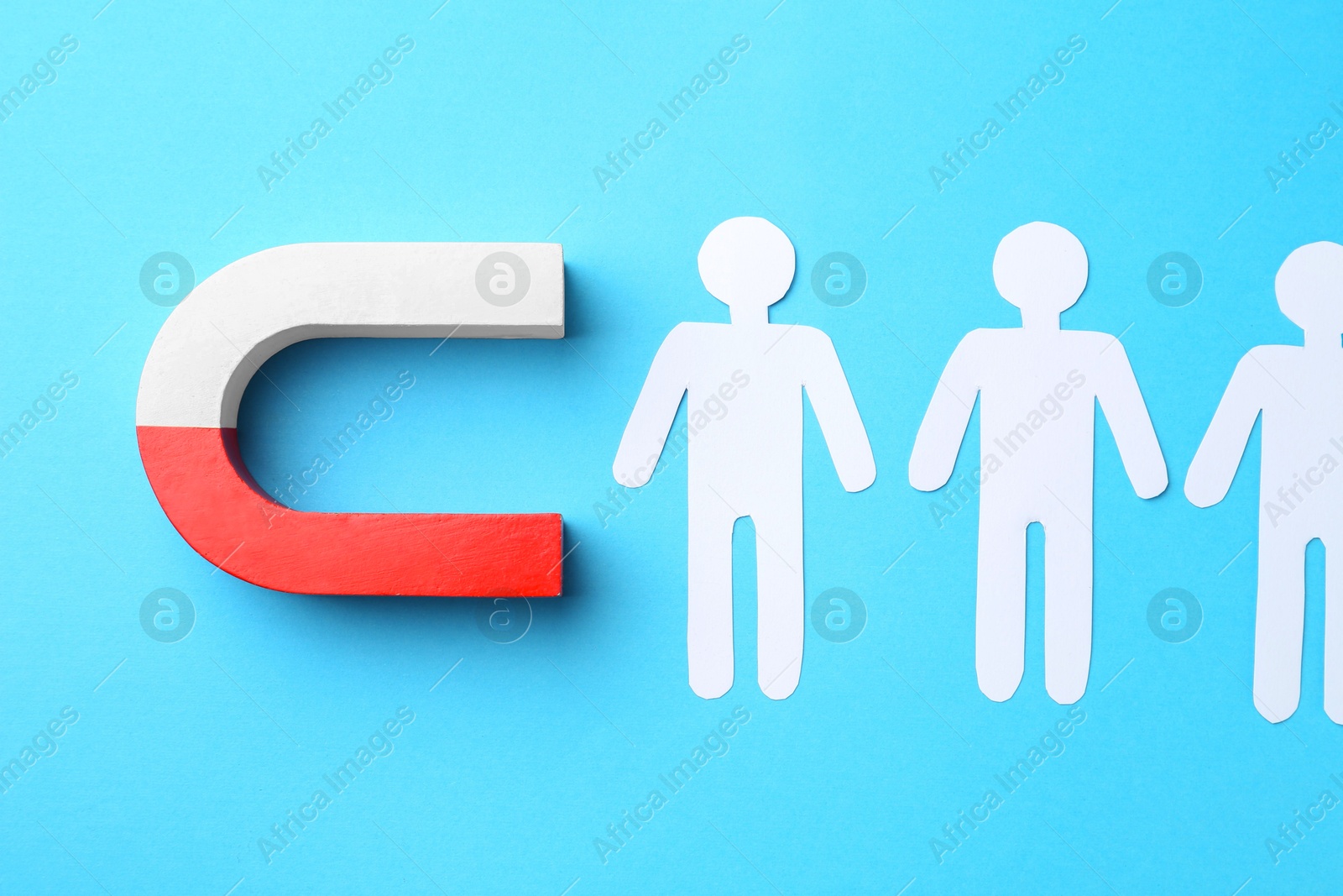 Photo of Magnet attracting paper cutouts of humans on light blue background, flat lay