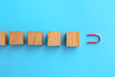 Photo of Magnet attracting wooden cubes on light blue background, flat lay