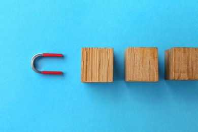 Photo of Magnet attracting wooden cubes on light blue background, flat lay