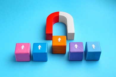 Photo of Magnet attracting colorful cubes on light blue background, closeup