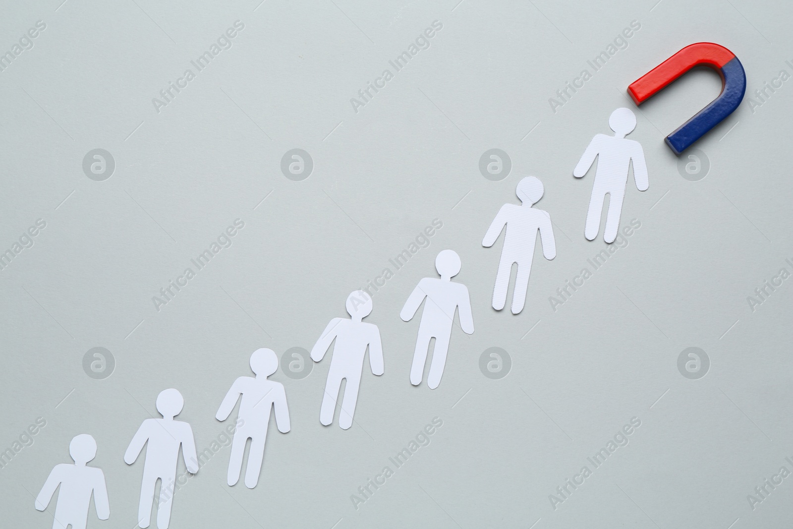 Photo of Magnet attracting paper cutouts of humans on light grey background, flat lay