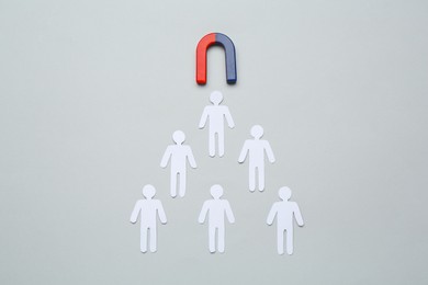 Photo of Magnet attracting paper cutouts of humans on light grey background, flat lay