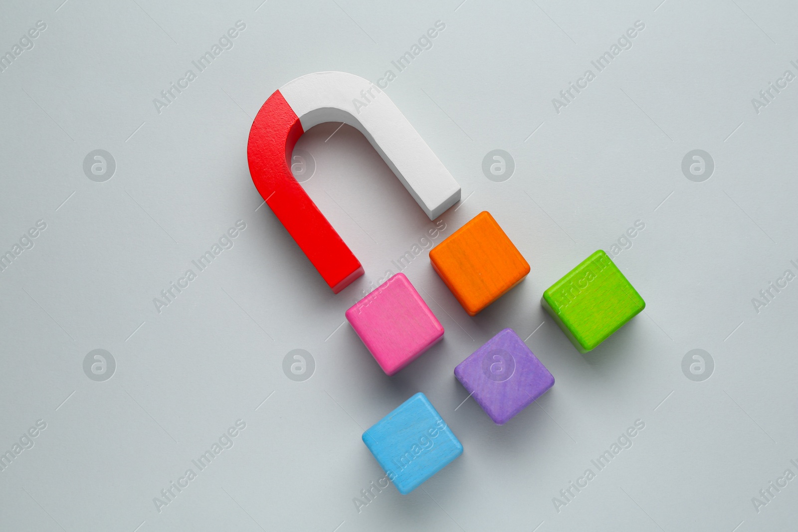 Photo of Magnet attracting colorful cubes on light grey background, flat lay