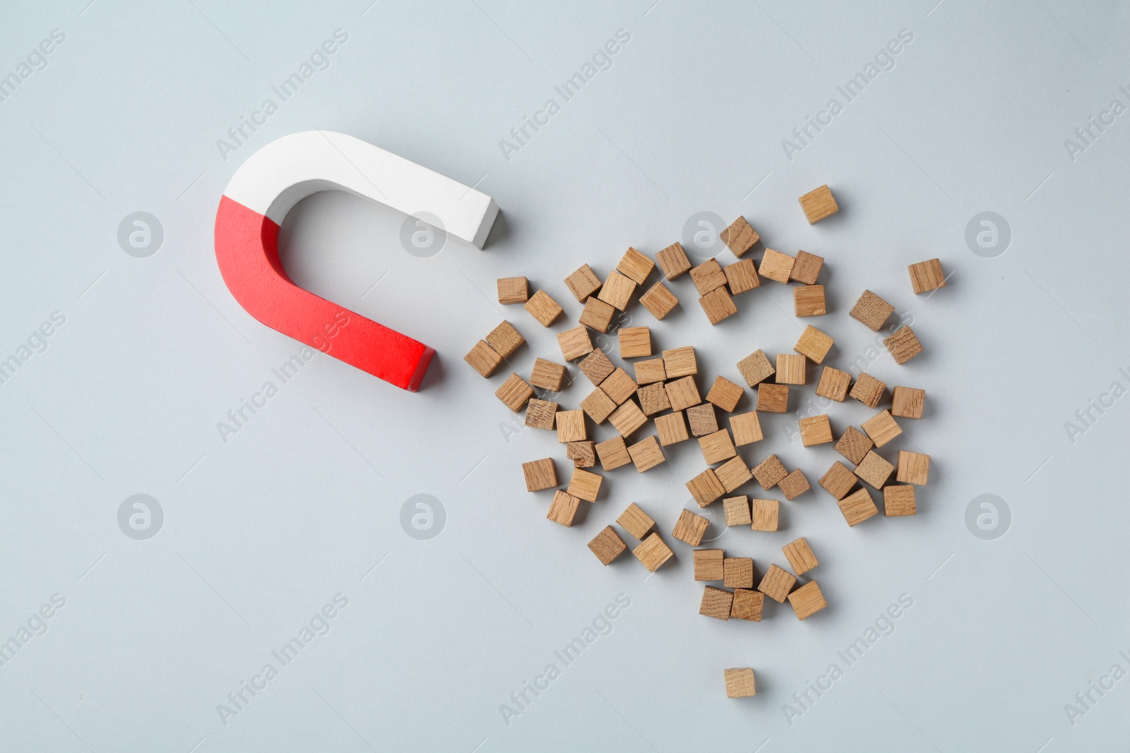 Photo of Magnet attracting wooden cubes on light grey background, flat lay