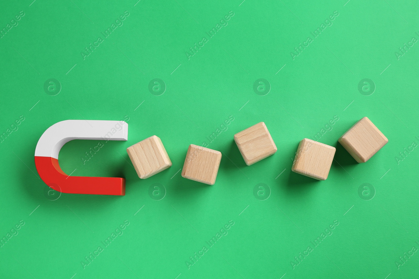 Photo of Magnet attracting wooden cubes on green background, flat lay