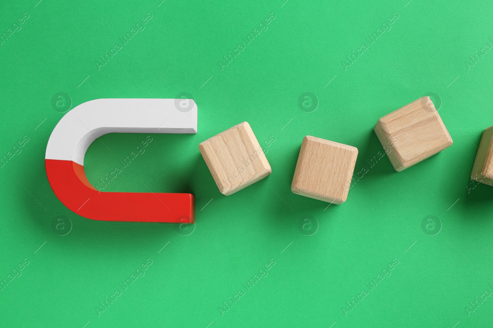 Photo of Magnet attracting wooden cubes on green background, flat lay