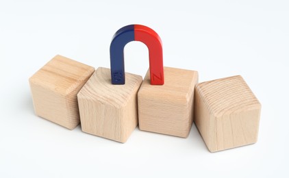 Photo of Magnet attracting wooden cubes on white background, closeup