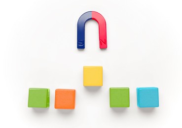 Photo of Magnet attracting colorful cubes on white background, flat lay