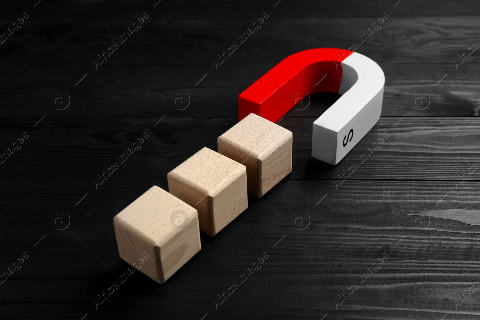 Photo of Magnet attracting cubes on black wooden table, closeup