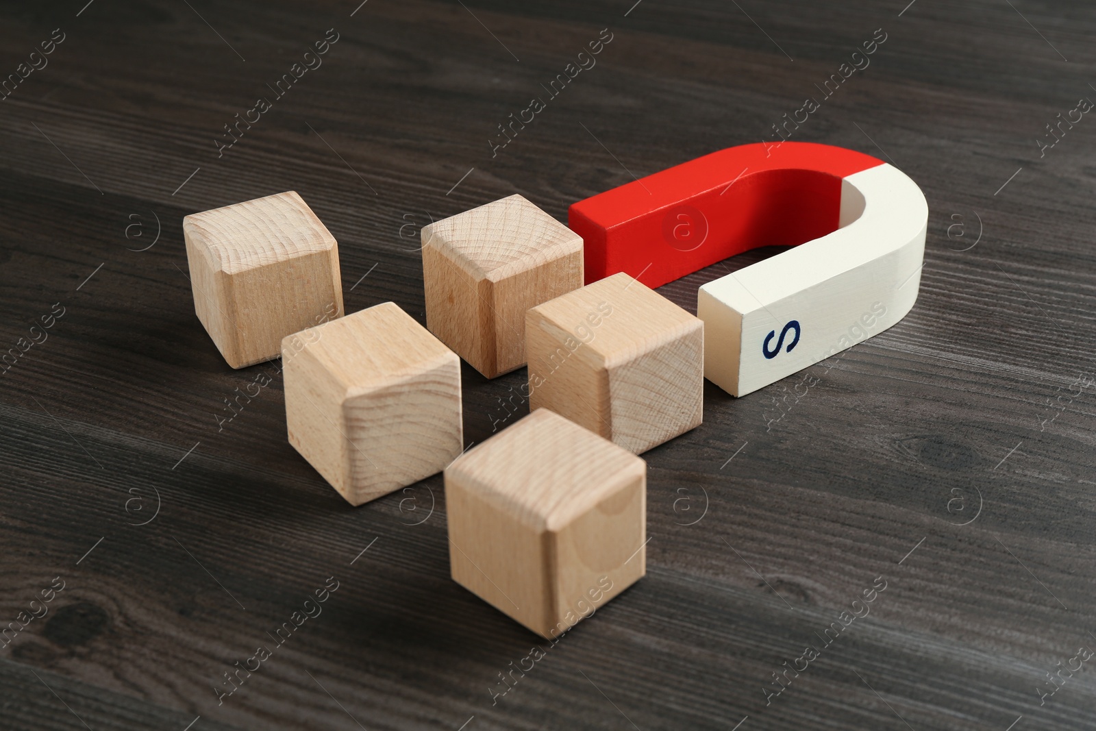 Photo of Magnet attracting cubes on wooden table, closeup