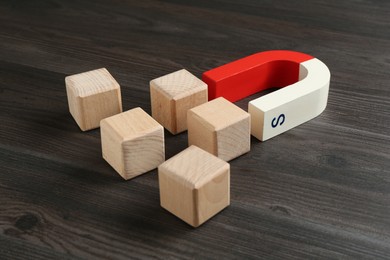 Photo of Magnet attracting cubes on wooden table, closeup