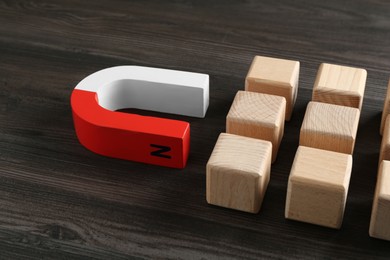 Photo of Magnet attracting cubes on wooden table, closeup