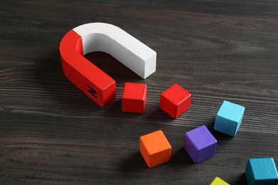 Photo of Magnet attracting with colorful cubes on wooden table, closeup