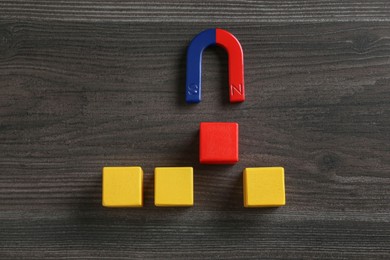 Photo of Magnet attracting red cube among yellow ones on wooden table, flat lay