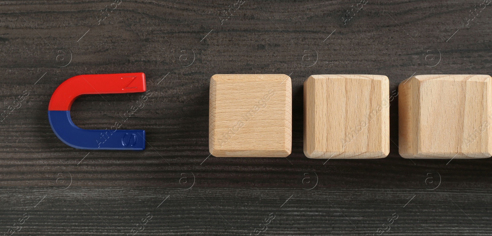 Photo of Magnet attracting cubes on wooden table, flat lay