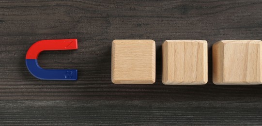 Photo of Magnet attracting cubes on wooden table, flat lay