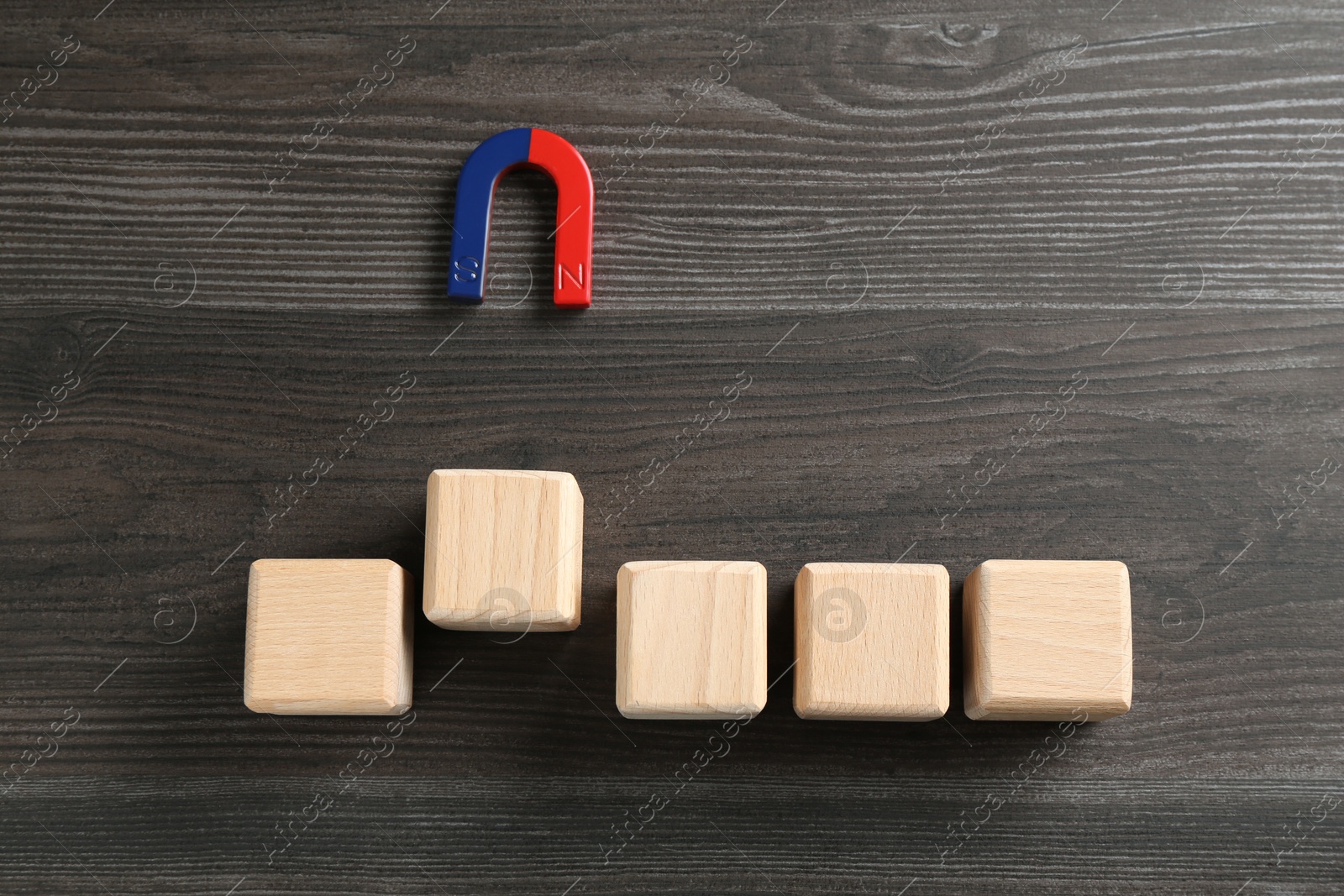 Photo of Magnet attracting cubes on wooden table, flat lay