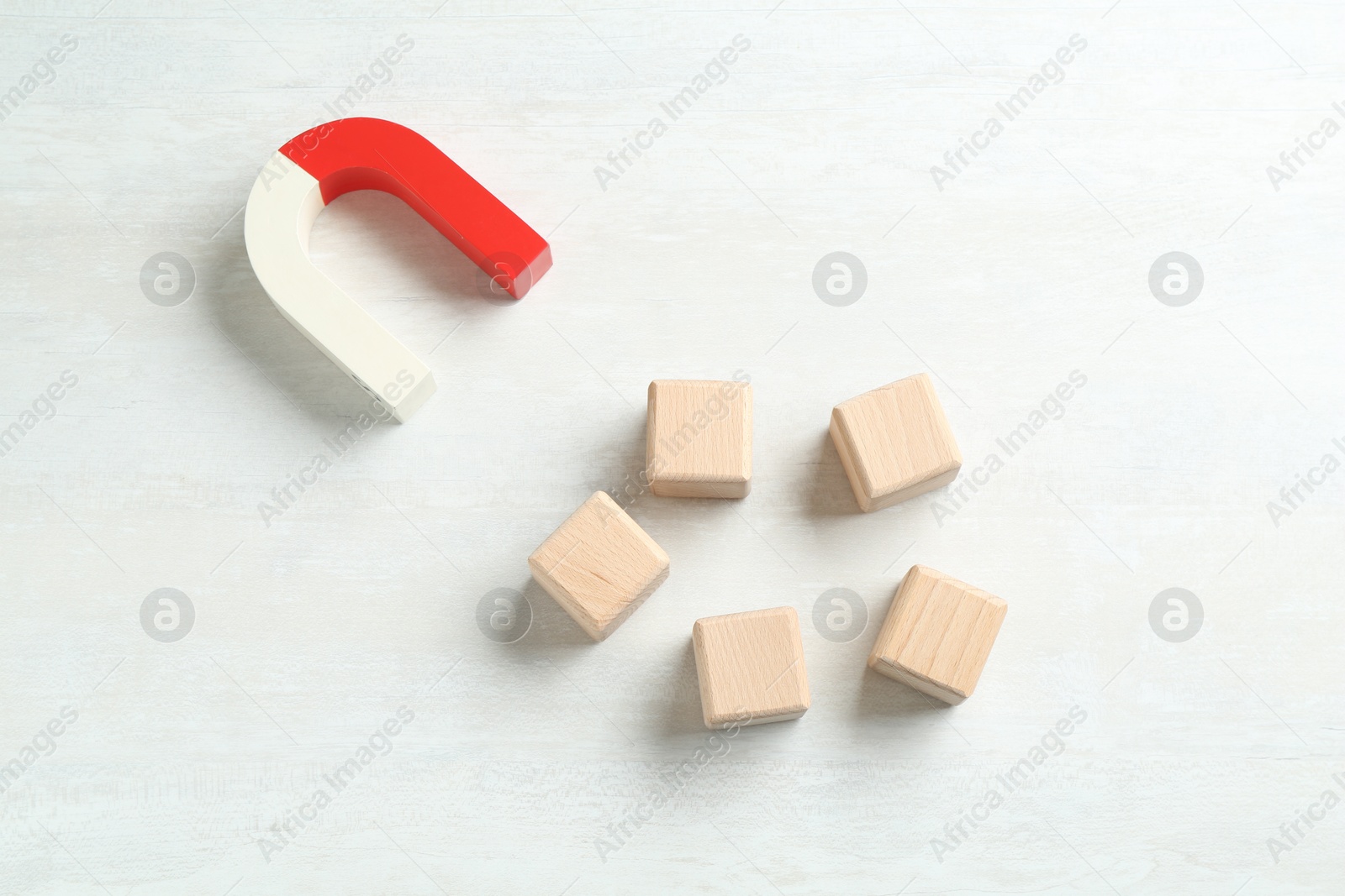 Photo of Magnet attracting wooden cubes on white table, flat lay