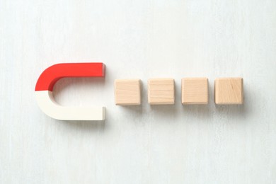 Photo of Magnet attracting wooden cubes on white table, flat lay