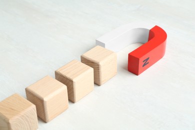 Photo of Magnet attracting wooden cubes on white table, closeup