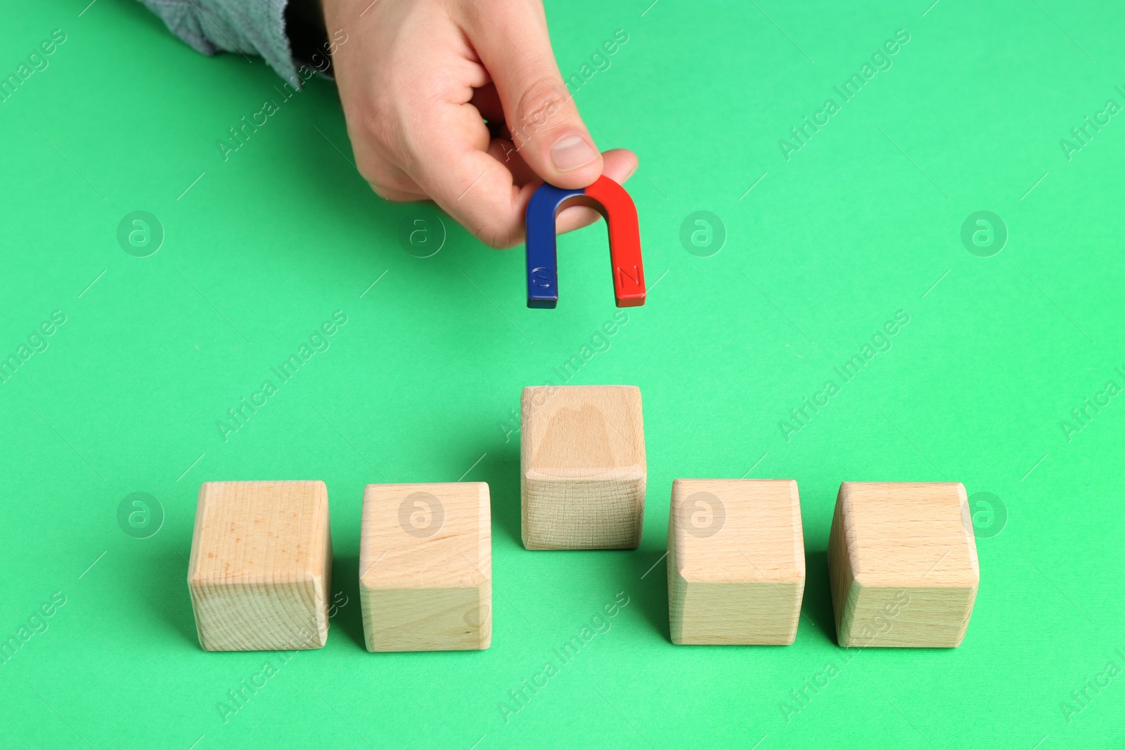 Photo of Man with magnet attracting wooden cubes at green table, closeup